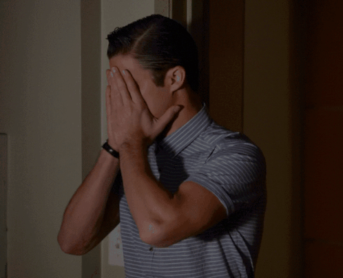 A Man Wearing A Striped Shirt Is Covering His Nose With His Hand GIF