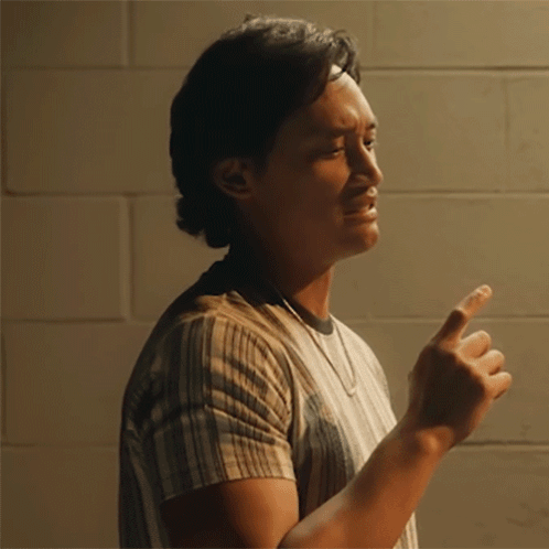 A Man Wearing A Striped Shirt Is Pointing At Something GIF