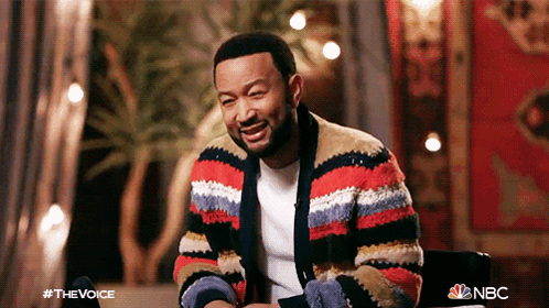 A Man Wearing A Striped Sweater Is Sitting In A Chair And Smiling GIF