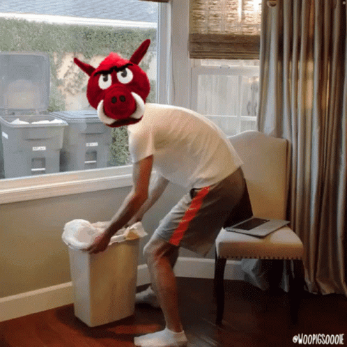 A Man Wearing A Stuffed Pig Head Throws A Trash Can GIF