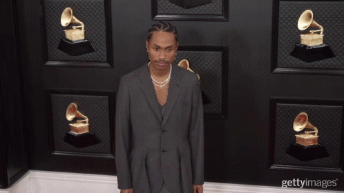 A Man Wearing A Suit And Pearls Stands In Front Of A Wall Of Grammophones GIF
