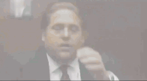 A Man Wearing A Suit And Tie Is Covering His Face With His Hand . GIF