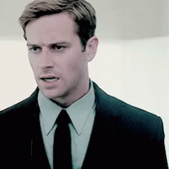 A Man Wearing A Suit And Tie Is Looking At The Camera . GIF