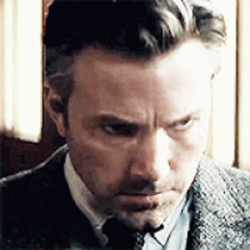 A Man Wearing A Suit And Tie Is Looking Down At Something . GIF