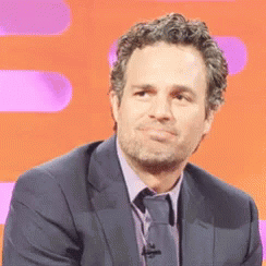 A Man Wearing A Suit And Tie Is Sitting In Front Of An Orange Background . GIF