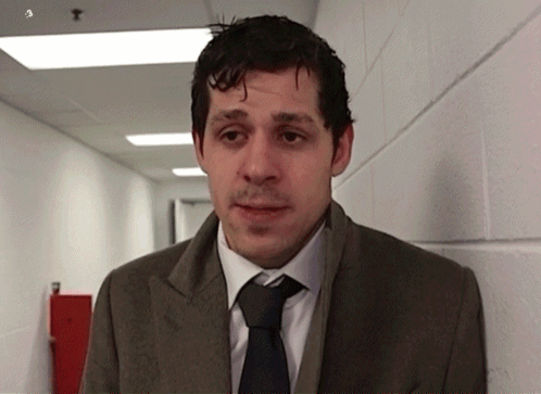 A Man Wearing A Suit And Tie Is Standing In A Hallway GIF
