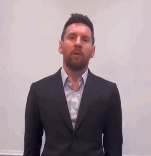 A Man Wearing A Suit And Tie Is Standing In Front Of A White Wall . GIF