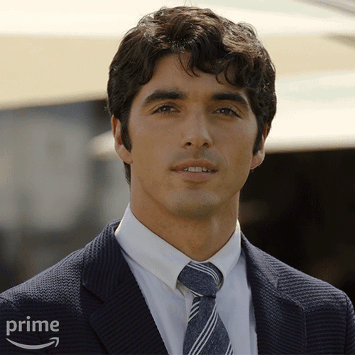 A Man Wearing A Suit And Tie Is Standing In Front Of An Amazon Prime Logo GIF