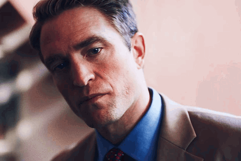 A Man Wearing A Suit And Tie Looks At The Camera GIF