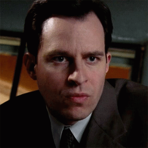 A Man Wearing A Suit And Tie Looks At The Camera GIF