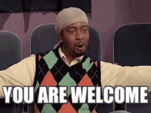A Man Wearing A Sweater And A Hat Is Sitting In A Theater . GIF