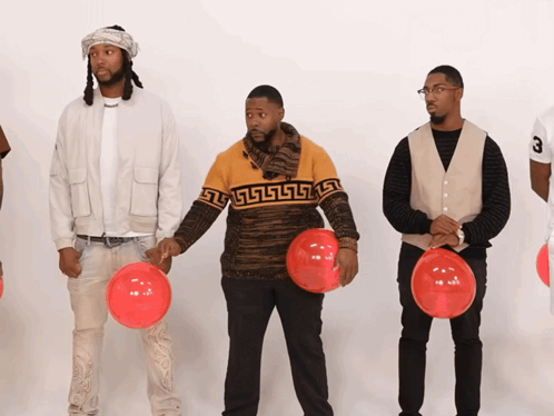 A Man Wearing A Sweater With A Greek Key Design Holds A Red Balloon GIF