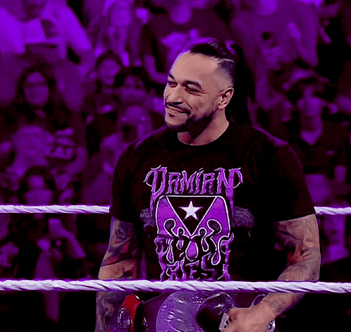 A Man Wearing A T-Shirt That Says Demon Reigns Stands In A Wrestling Ring GIF