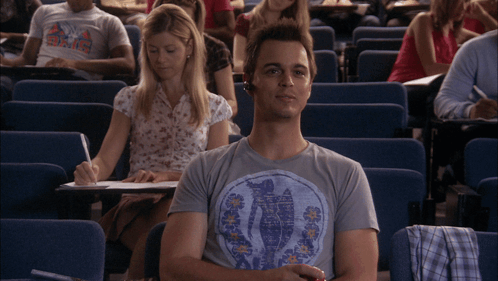 A Man Wearing A T-Shirt That Says ' Hawaii ' On It Sits In A Lecture Hall With Other Students GIF