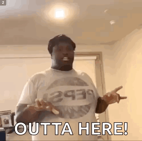 A Man Wearing A T-Shirt That Says Outta Here Is Standing In A Room With His Hands Outstretched . GIF
