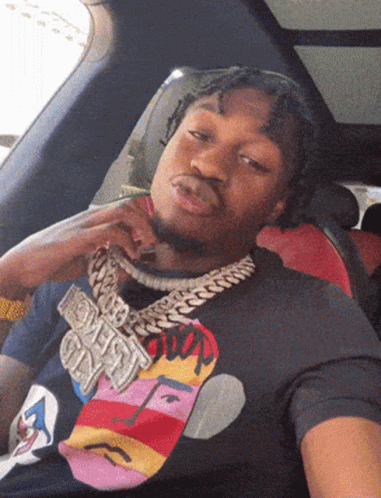 A Man Wearing A T-Shirt With A Face On It Is Sitting In A Car With His Hand On His Face GIF