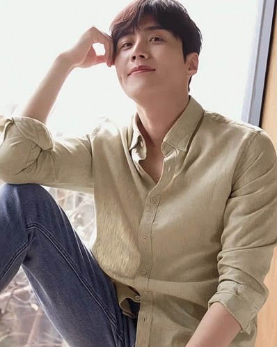 A Man Wearing A Tan Shirt And Blue Jeans Sits On The Floor GIF