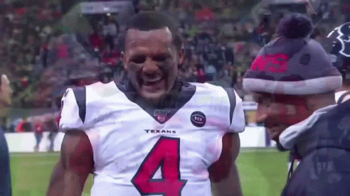 A Man Wearing A Texans Jersey Is Standing On A Football Field With His Mouth Open . GIF
