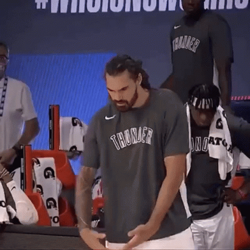 A Man Wearing A Thunder T-Shirt Is Standing Next To Another Man . GIF