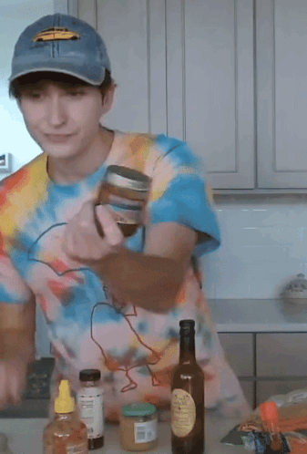 A Man Wearing A Tie Dye Shirt And A Blue Hat Is Standing In A Kitchen GIF