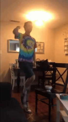 A Man Wearing A Tie Dye Shirt Is Dancing In A Living Room GIF