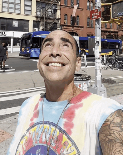A Man Wearing A Tie Dye Shirt Is Smiling In Front Of A Sign That Says No Wrong Way GIF