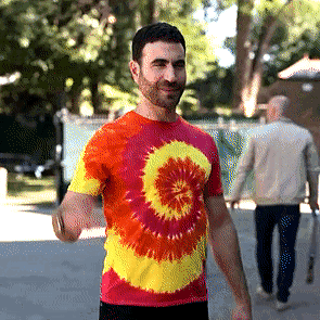 A Man Wearing A Tie Dye Shirt Is Walking Down A Street GIF