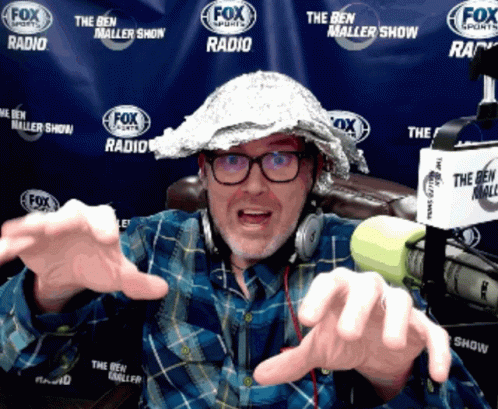 A Man Wearing A Tin Foil Hat And Headphones Is In Front Of A Fox Sports Banner GIF