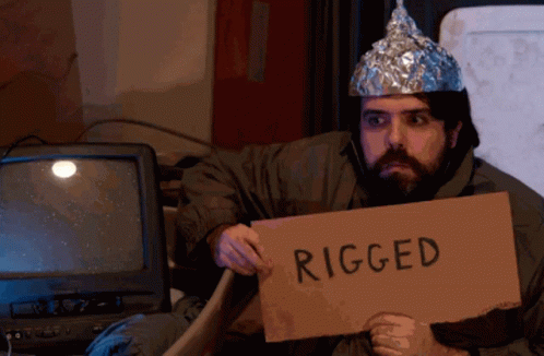 A Man Wearing A Tin Foil Hat Holds A Cardboard Sign That Says Rigged GIF