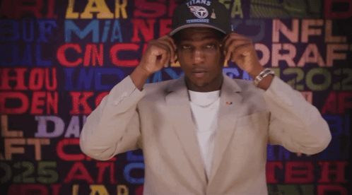 a man wearing a titans hat stands in front of a wall of nfl draft logos