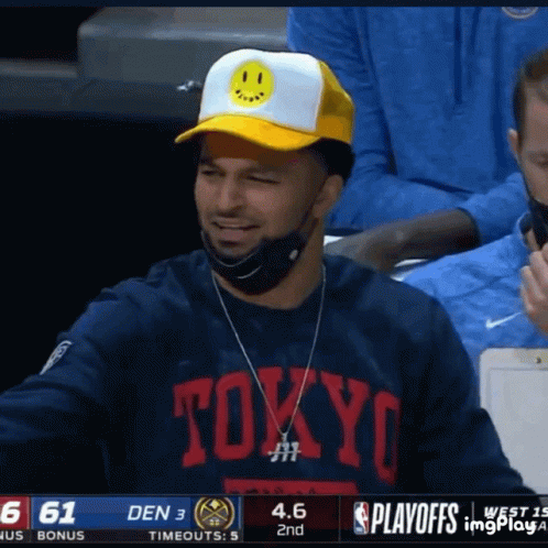 A Man Wearing A Tokyo Shirt And A Yellow Hat Smiles During A Basketball Game GIF