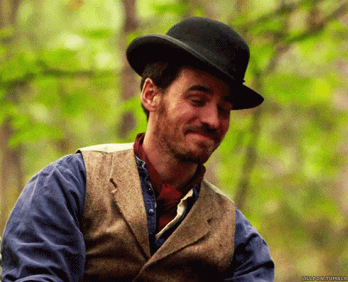 A Man Wearing A Top Hat And A Vest Smiles In Front Of Trees GIF