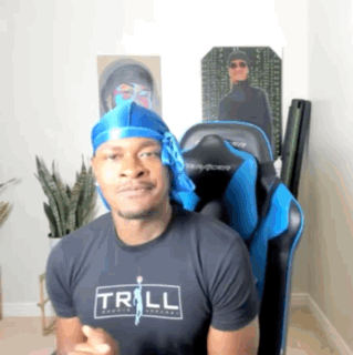 A Man Wearing A Trill T-Shirt Is Sitting In A Gaming Chair GIF
