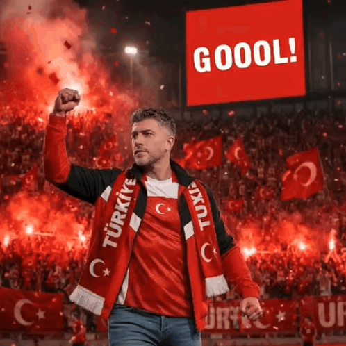 a man wearing a turkey scarf stands in front of a large screen that says goool