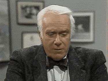 A Man Wearing A Tuxedo And Bow Tie Is Looking Down . GIF