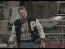 Man In Varsity Jacket Standing By Fence GIF