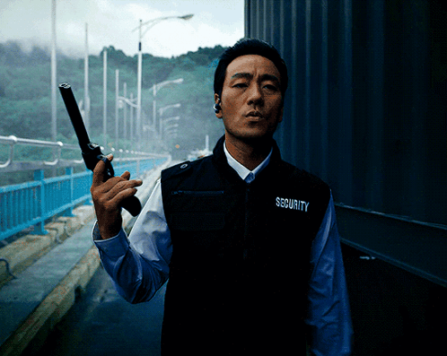 A Man Wearing A Vest That Says Security On It Holds A Gun GIF