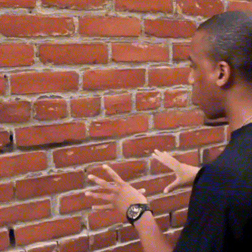 A Man Wearing A Watch Is Standing In Front Of A Brick Wall With His Hands Outstretched GIF