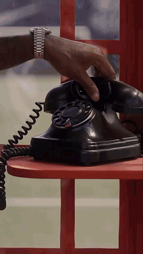 A Man Wearing A Watch Is Talking On A Black Telephone GIF