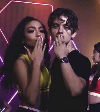A Man Wearing A Watch Stands Next To A Woman Who Is Covering Her Mouth With Her Hand GIF
