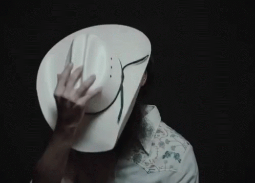 A Man Wearing A White Cowboy Hat Is Covering His Face With It GIF