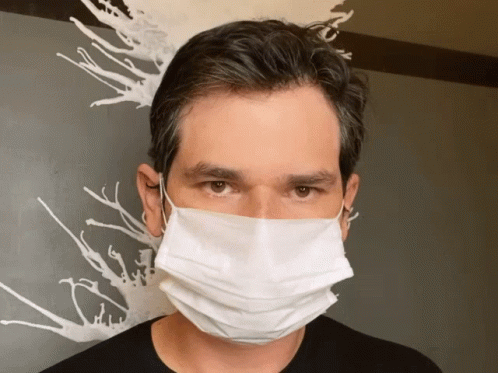 A Man Wearing A White Face Mask Stands In Front Of A Painting GIF