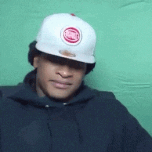 A Man Wearing A White Hat And A Black Hoodie Is Making A Face . GIF