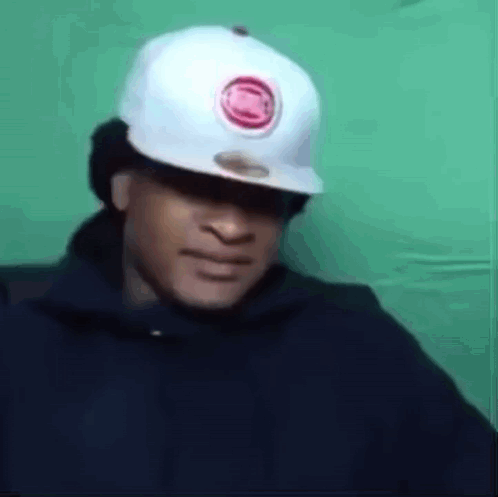A Man Wearing A White Hat And A Black Hoodie Is Making A Funny Face . GIF