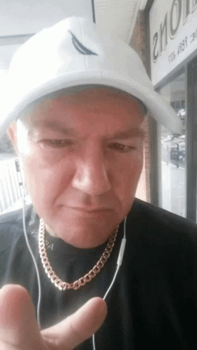 a man wearing a white hat and a gold chain is giving the thumbs up sign