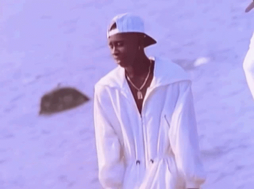 A Man Wearing A White Hat And A White Jacket Is Standing On The Beach . GIF