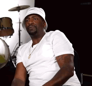 A Man Wearing A White Hat And A White Shirt Sits In Front Of A Drum Set GIF