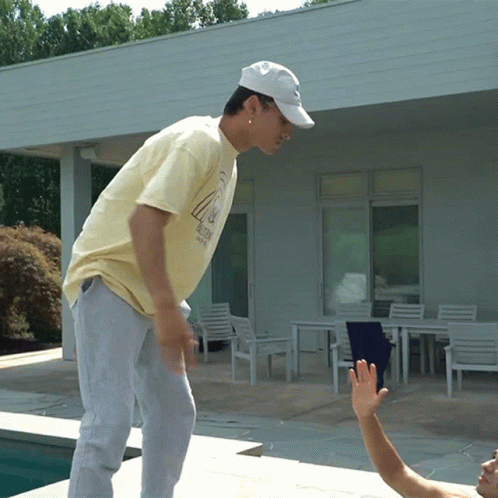 A Man Wearing A White Hat And A Yellow Shirt With The Number 4 On It Stands Near A Pool GIF