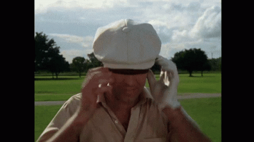 A Man Wearing A White Hat And Gloves Is Standing In A Park GIF