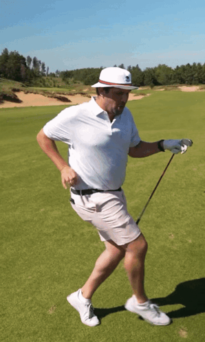 A Man Wearing A White Hat Is Holding A Golf Club On A Golf Course GIF